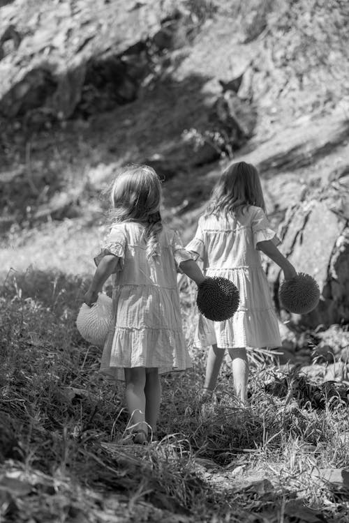 Two Girls Wearing Dresses Walking on Grass