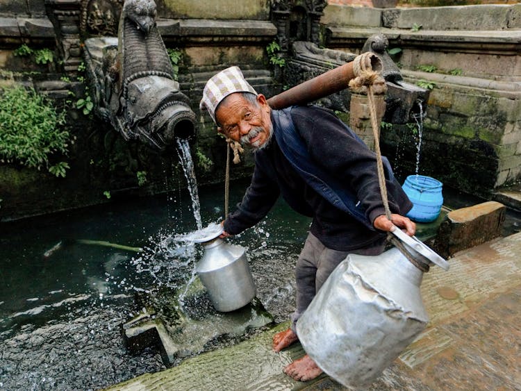 Elderly Man Filling Metal Jars With Water 