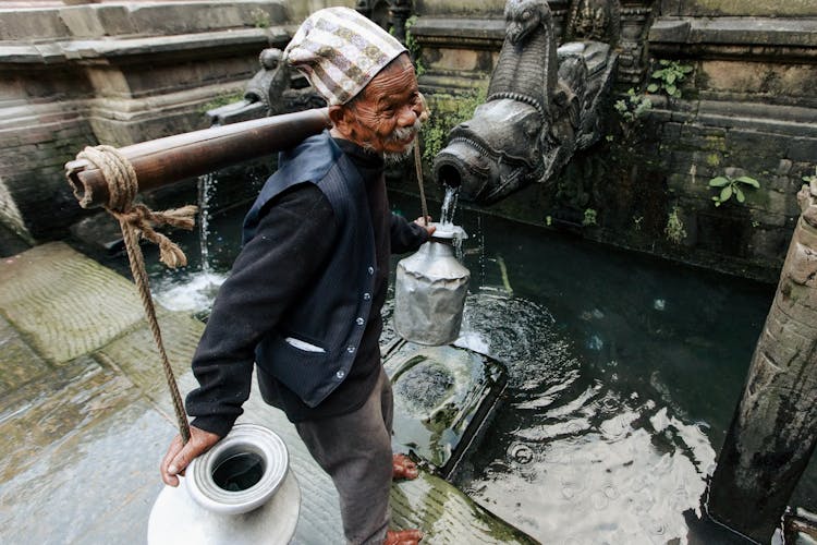 Elderly Man Filling Metal Jars With Water 