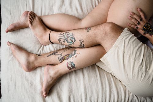 Free Close-up of tattooed legs of a couple entwined on a bed, expressing intimacy and relaxation. Stock Photo