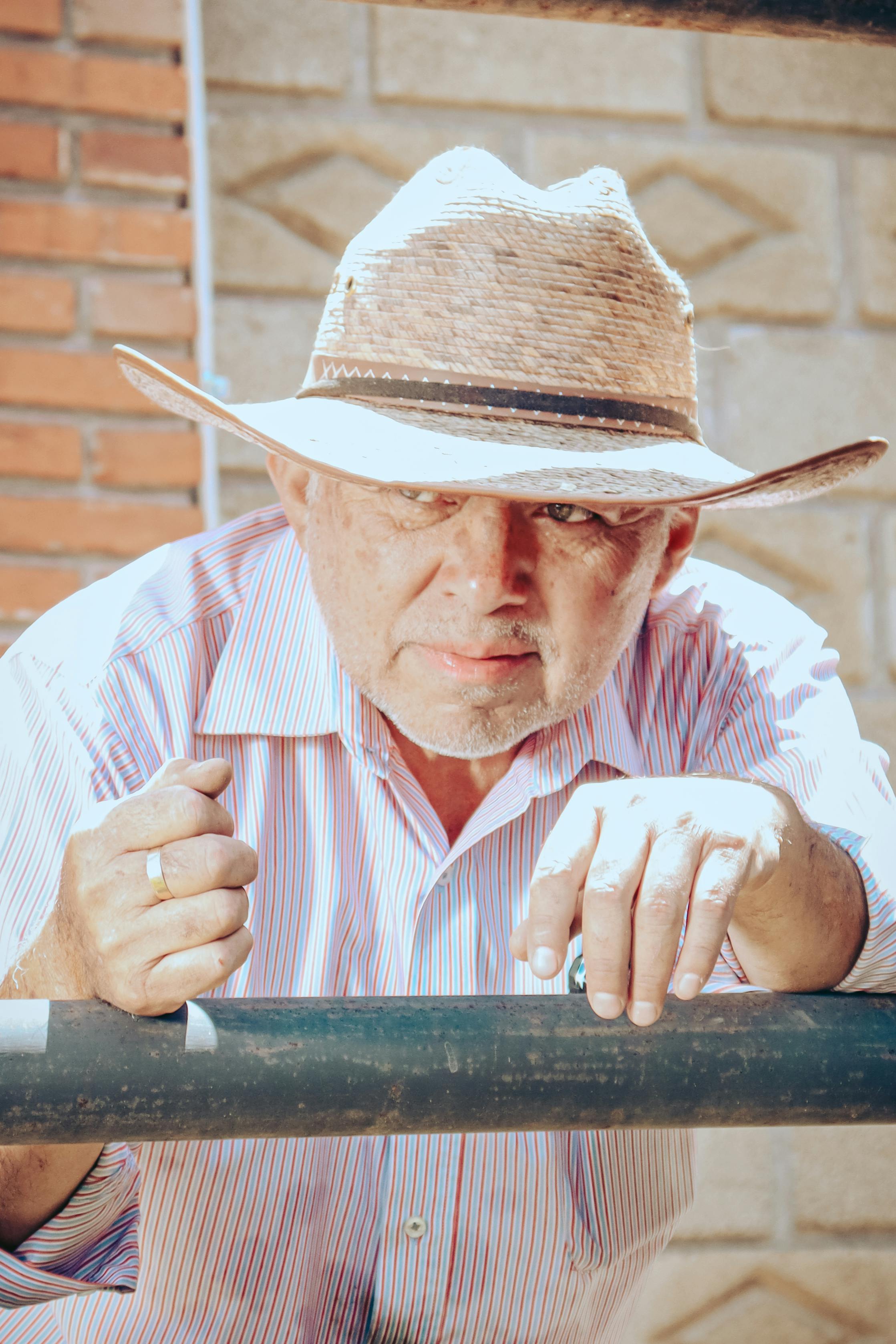 Elderly man leaning on a metal railing wearing a straw hat and striped shirt in Mexico.
