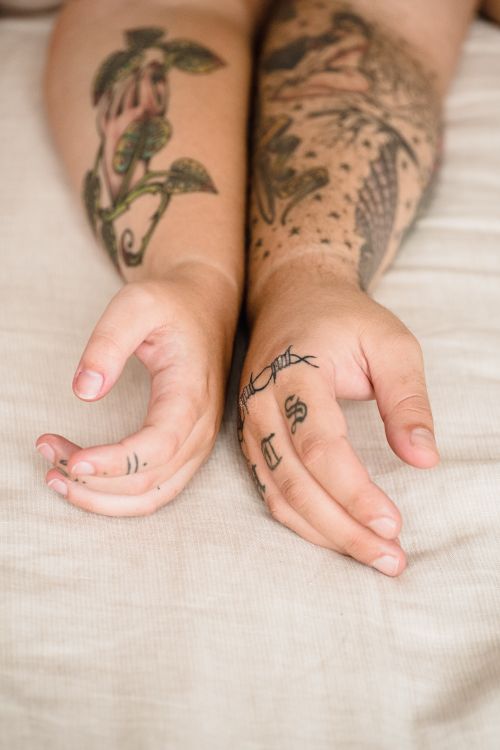 Free Close-up of two tattooed arms and hands resting on a light fabric. Stock Photo
