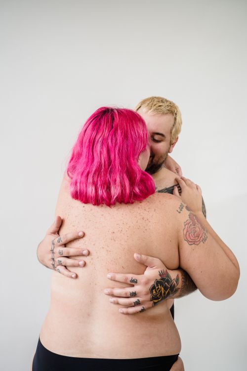 Free Body-positive embrace showcasing diversity and love, highlighted by vibrant tattoos and pink hair. Stock Photo