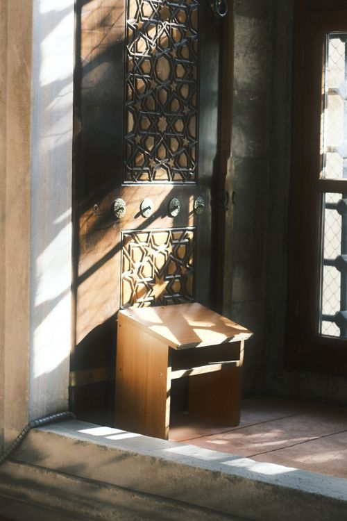 Free A sunlit antique wooden chair is placed next to an intricately designed door, casting beautiful shadows. Stock Photo