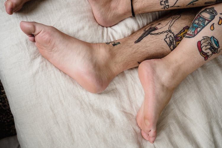 Close-up Of Couple Legs With Tattoos In Bed