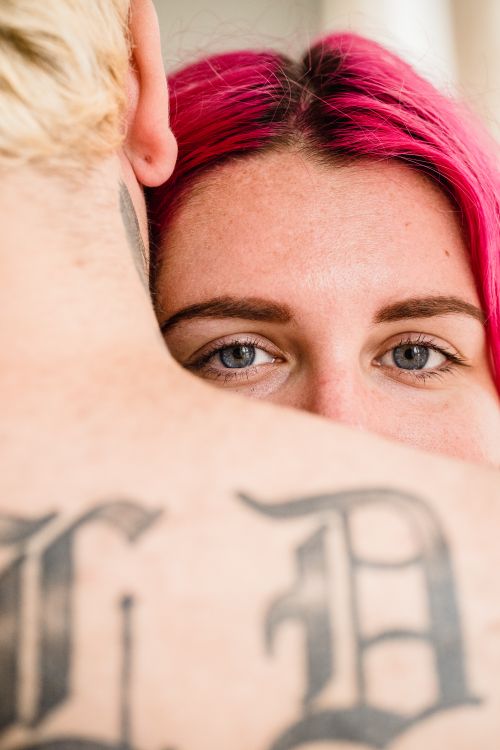 Free An intimate close-up of a couple embracing, showcasing tattoos and vibrant pink hair. Stock Photo