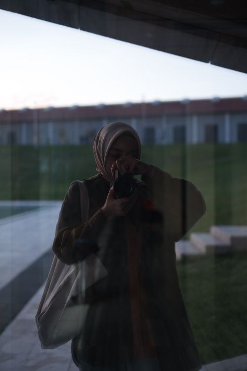 Free A woman in a headscarf takes a photo through a window reflection. Stock Photo