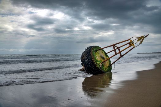 Stranded buoy with moss on Torremolinos beach under a cloudy sky.
