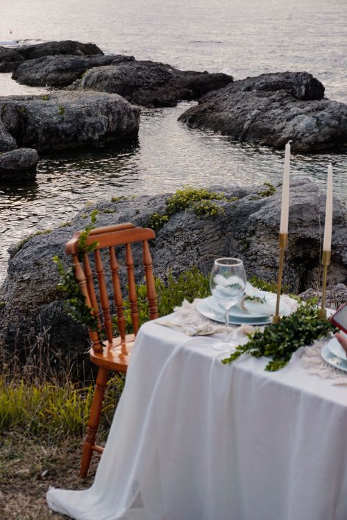 Free Stylish outdoor dining setup by a rocky shoreline in Turkey, perfect for intimate gatherings. Stock Photo