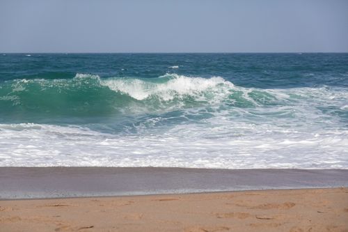 Free Ocean waves crash on a sandy beach under a clear sky, evoking a serene summer day. Stock Photo