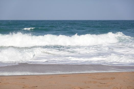 Vibrant ocean waves crashing onto a sandy beach under a clear blue sky.