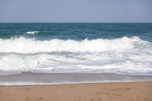 Free Vibrant ocean waves crashing onto a sandy beach under a clear blue sky. Stock Photo