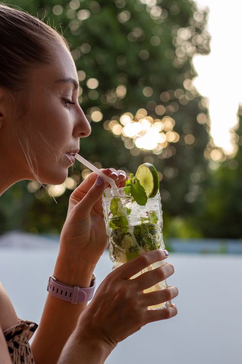 Free Young woman enjoying a fresh mint lime cocktail outdoors during sunset. Stock Photo