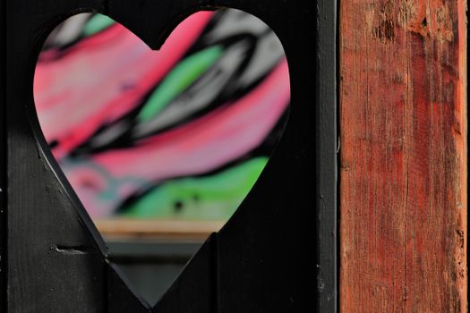 Vibrant graffiti seen through a heart-shaped cut in a wooden fence, capturing urban art in Cape Town.