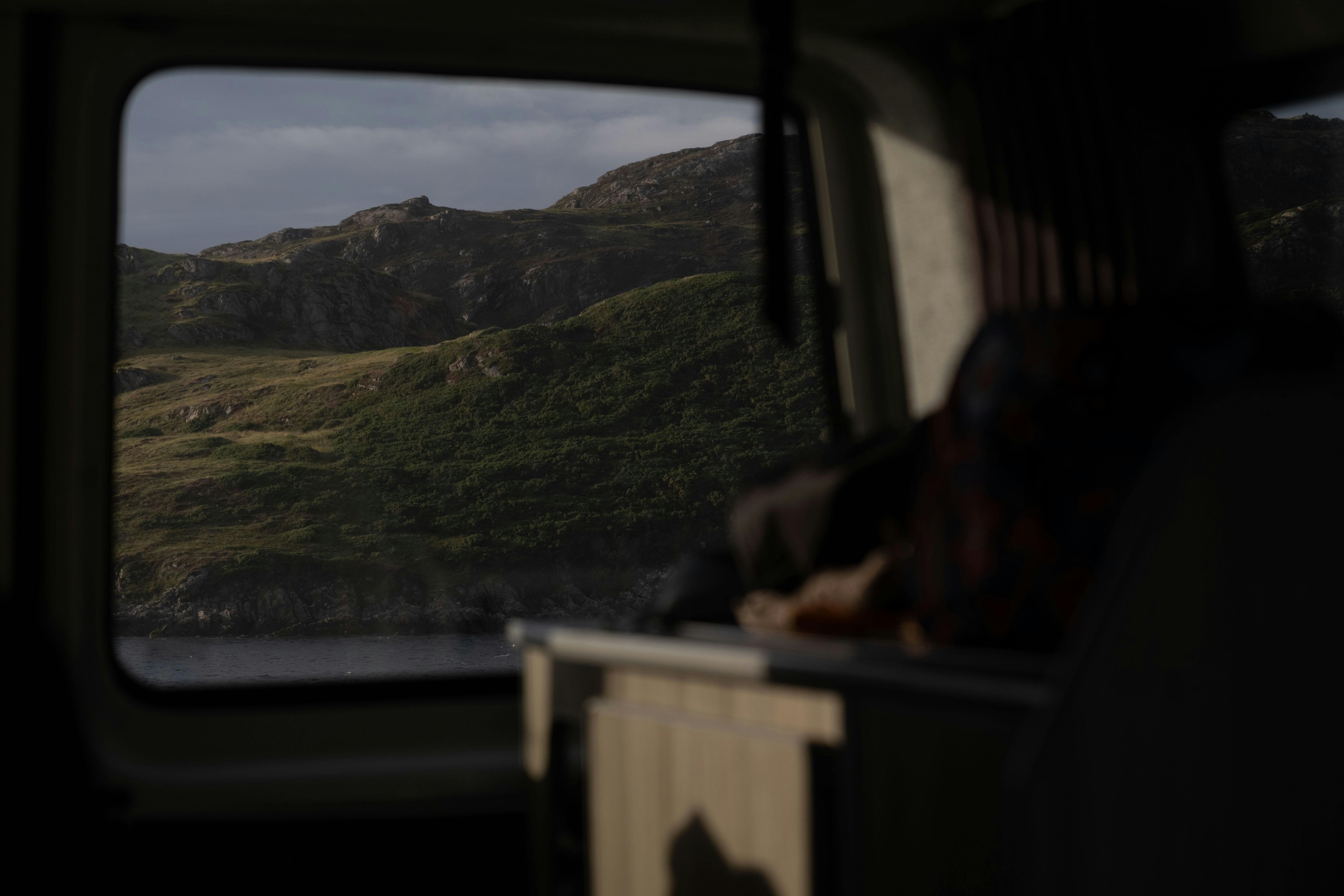 Serene view of a lush hillside landscape seen through a car window, capturing nature's calm beauty.