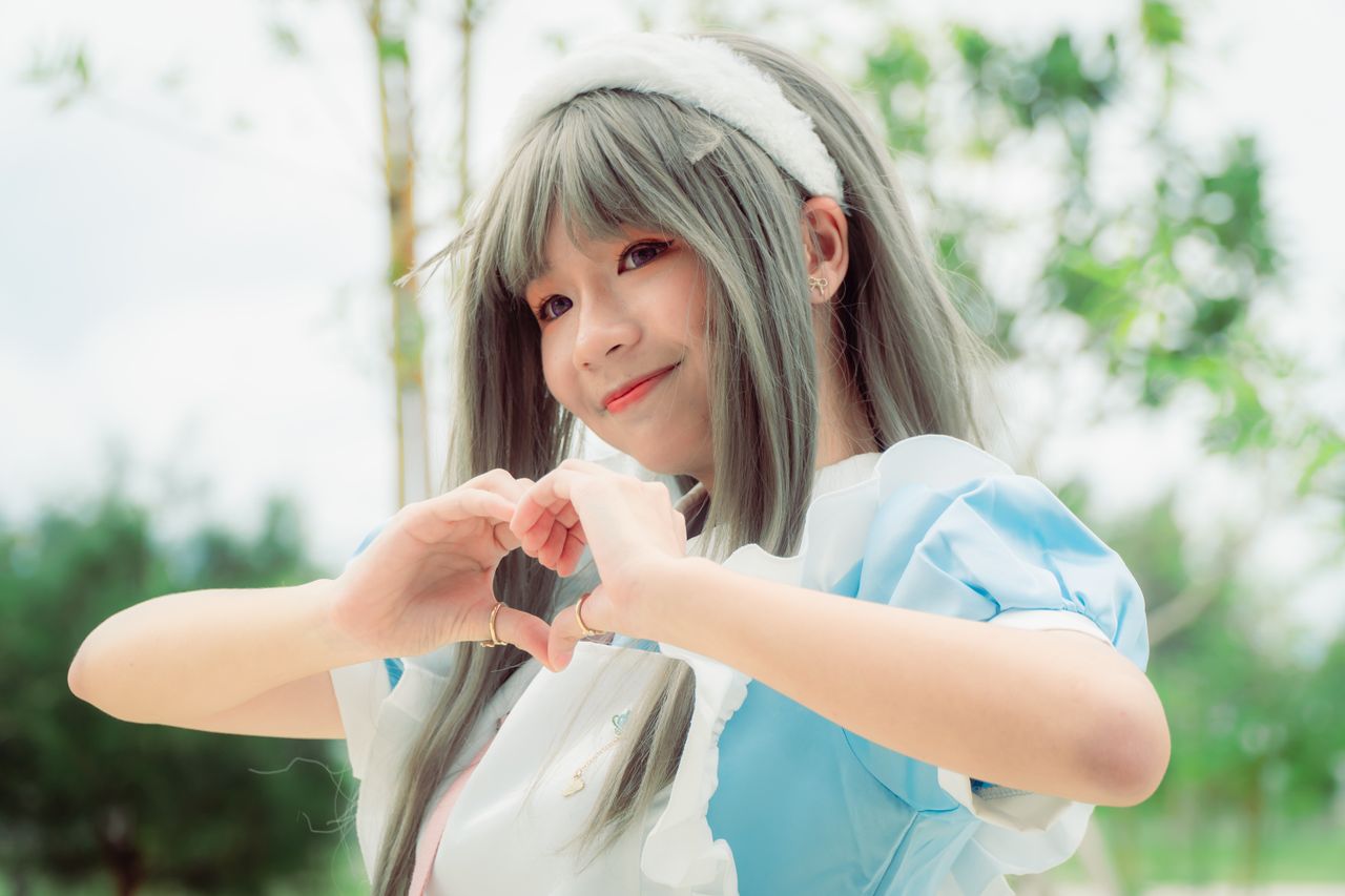 a young woman cosplayer in a blue costume outdoors creating a heart sh
