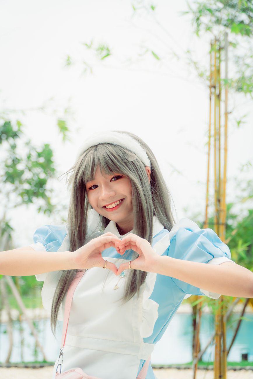 Cheerful woman with dyed hair making a heart gesture while posing outdoors under clear skies.