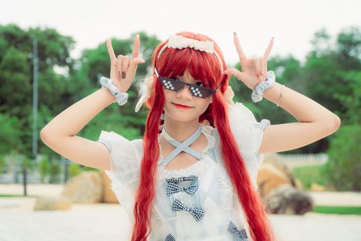 Young woman with red hair and pixel sunglasses in playful cosplay pose outdoors.