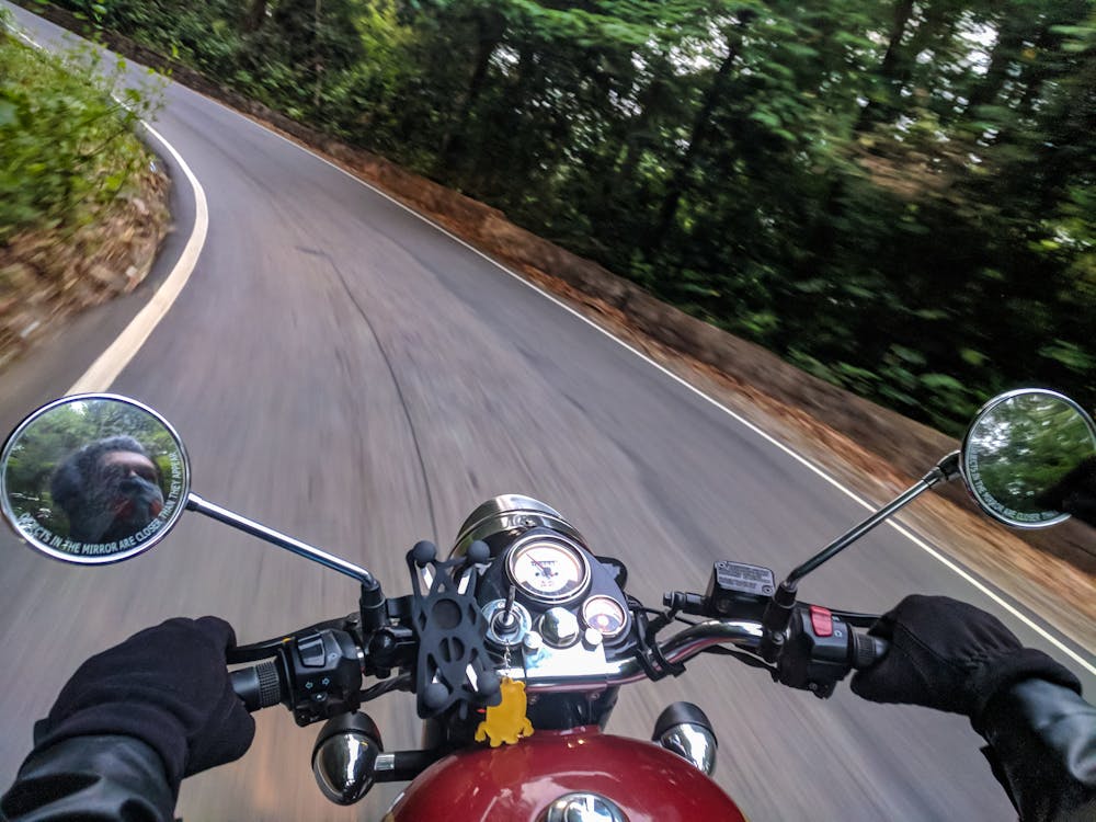 Person driving a motorcycle on a curved concrete road near trees