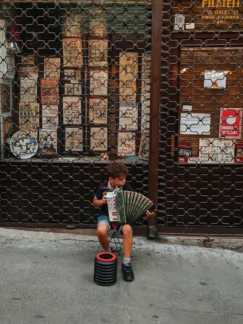 Boy Sitting on Chair Near Fence Playing Music