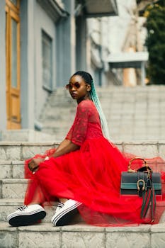 Fashionable woman in vibrant red dress on city stairs, embracing modern style.