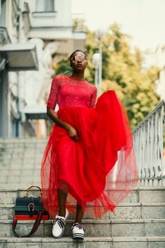 Stylish woman in a bold red dress posing on a city staircase, embodying urban fashion.