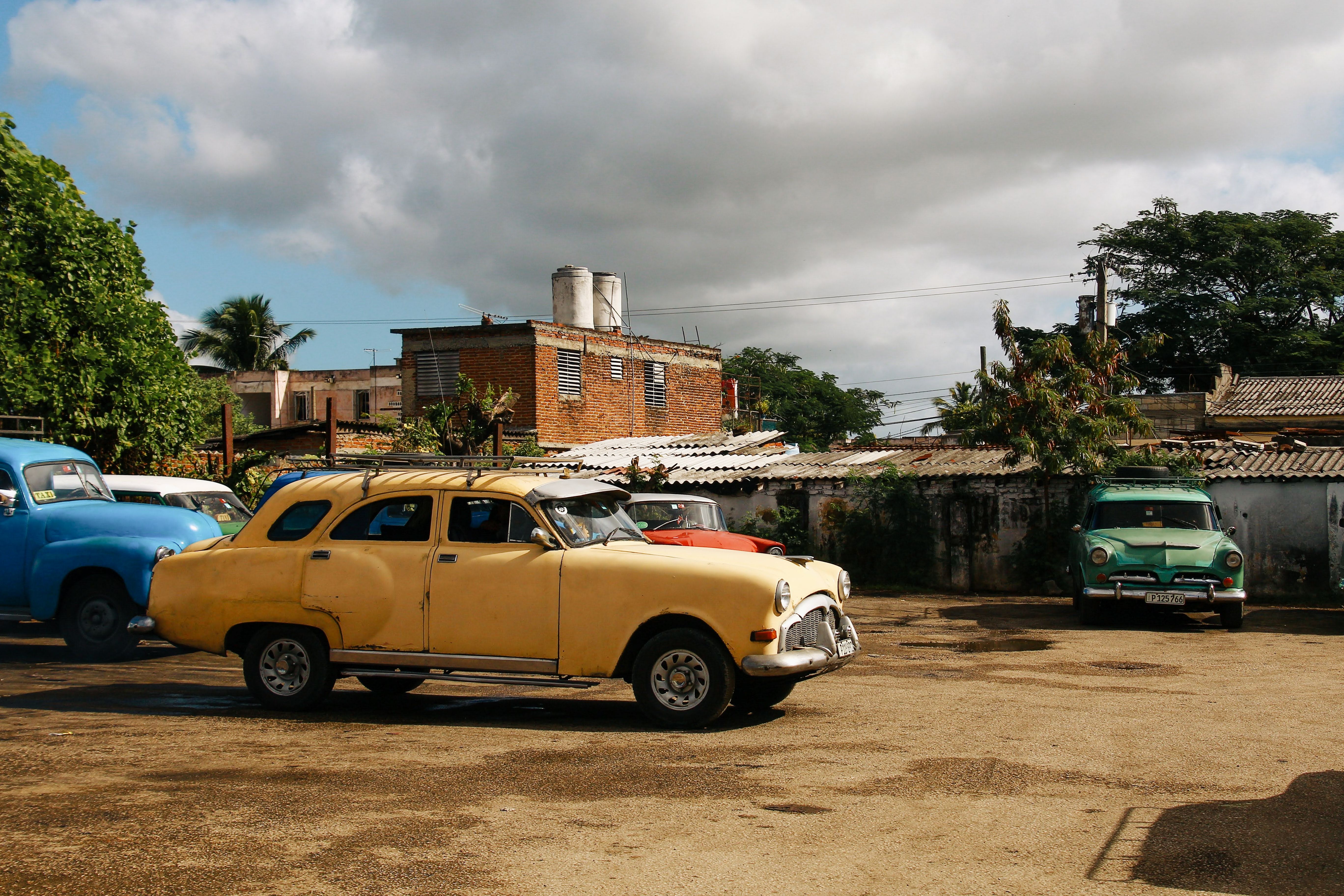 A collection of classic vintage cars in a parking lot under a cloudy sky.