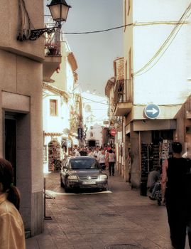 Charming narrow street view in Tossa de Mar, Spain with pedestrians and local architecture.
