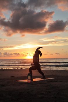 Silhouette of a woman doing yoga on the beach during sunset, creating a serene and calming scene.