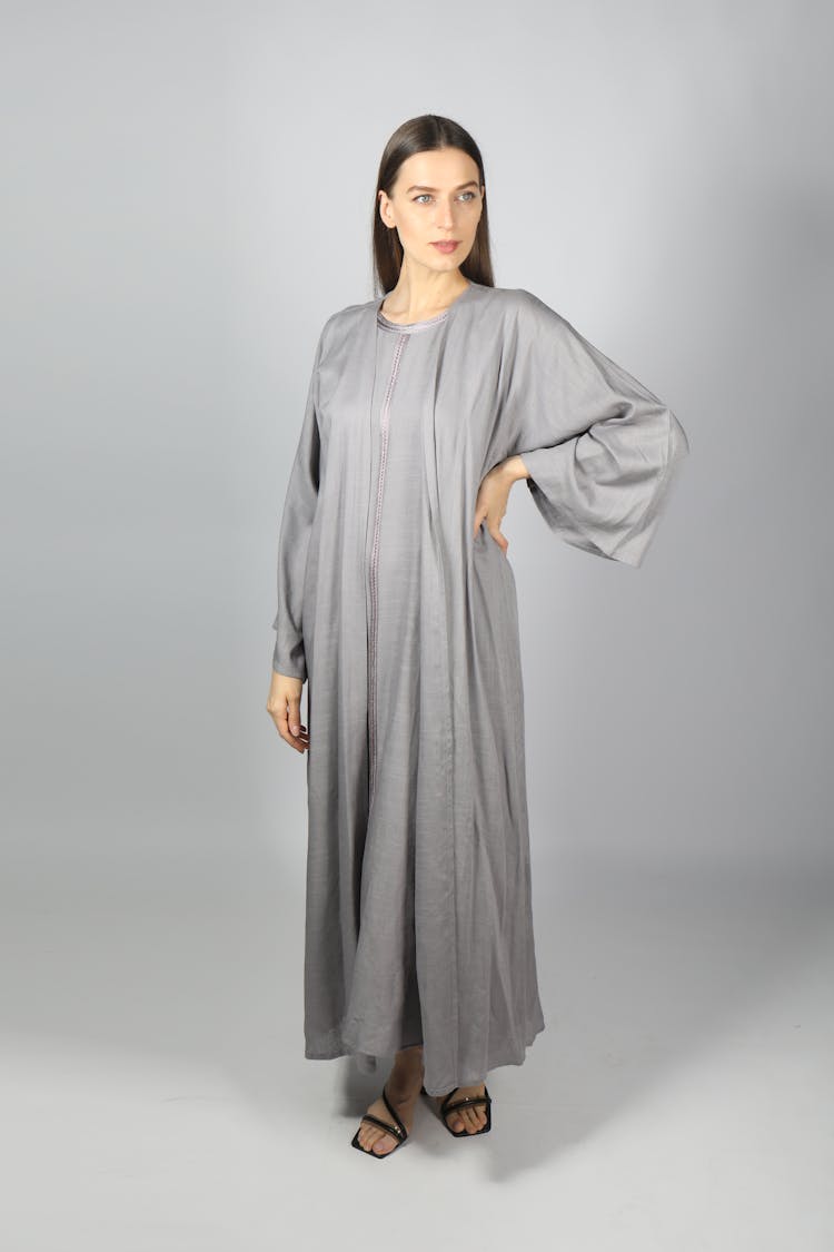 A Woman Wearing Gray Abaya Standing Near White Background While Looking Afar