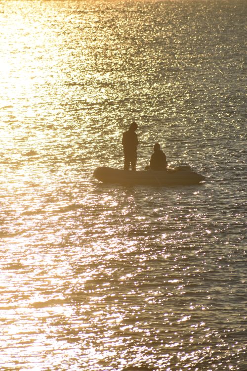 Free Two men silhouette fishing on a calm sea in Monopoli, Italy during golden hour. Stock Photo