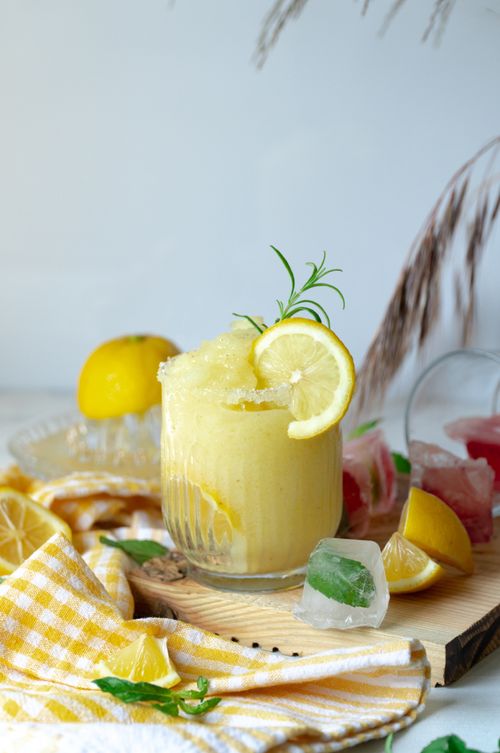 Free Close-up of a lemon sherbet in a glass with ice cubes, garnished with fresh rosemary and lemon slice. Stock Photo