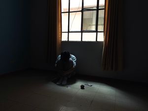 A person sitting alone on the floor of a dim room by a barred window &mdash; photo by Enzo Mej&iacute;a on Pexels