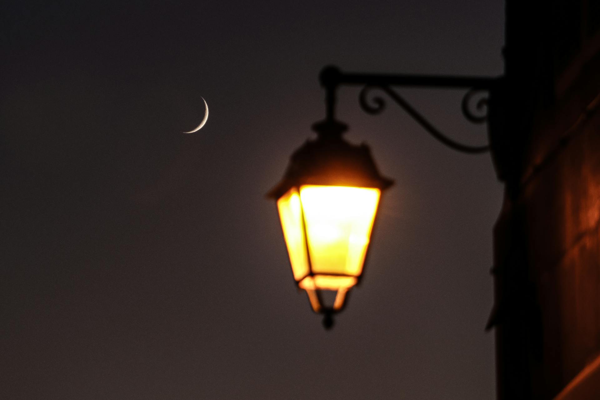 A vintage lamp illuminates the night sky with a crescent moon in Clermont-Ferrand, France.