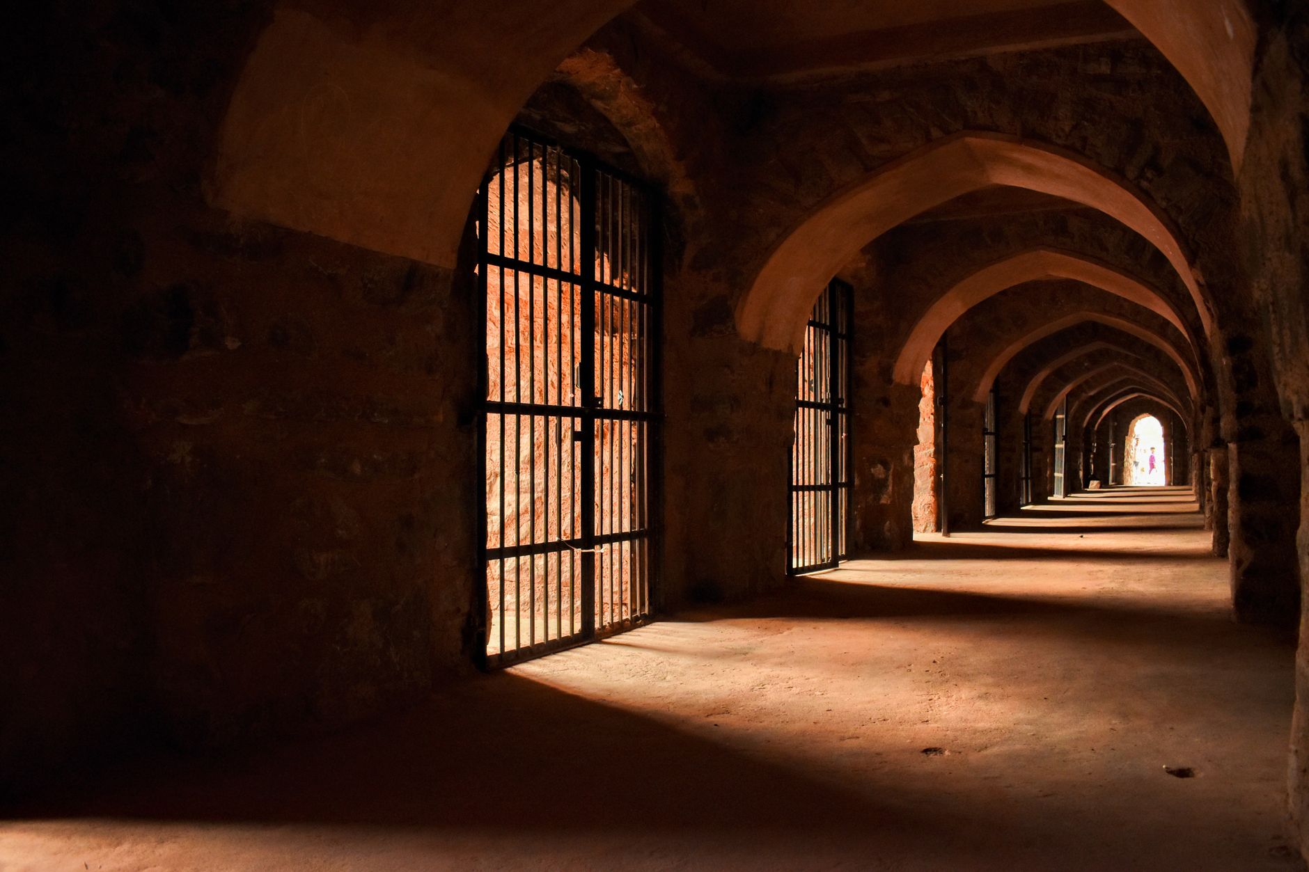 Dramatic lighting in an ancient stone corridor with gothic arches and barred gates.