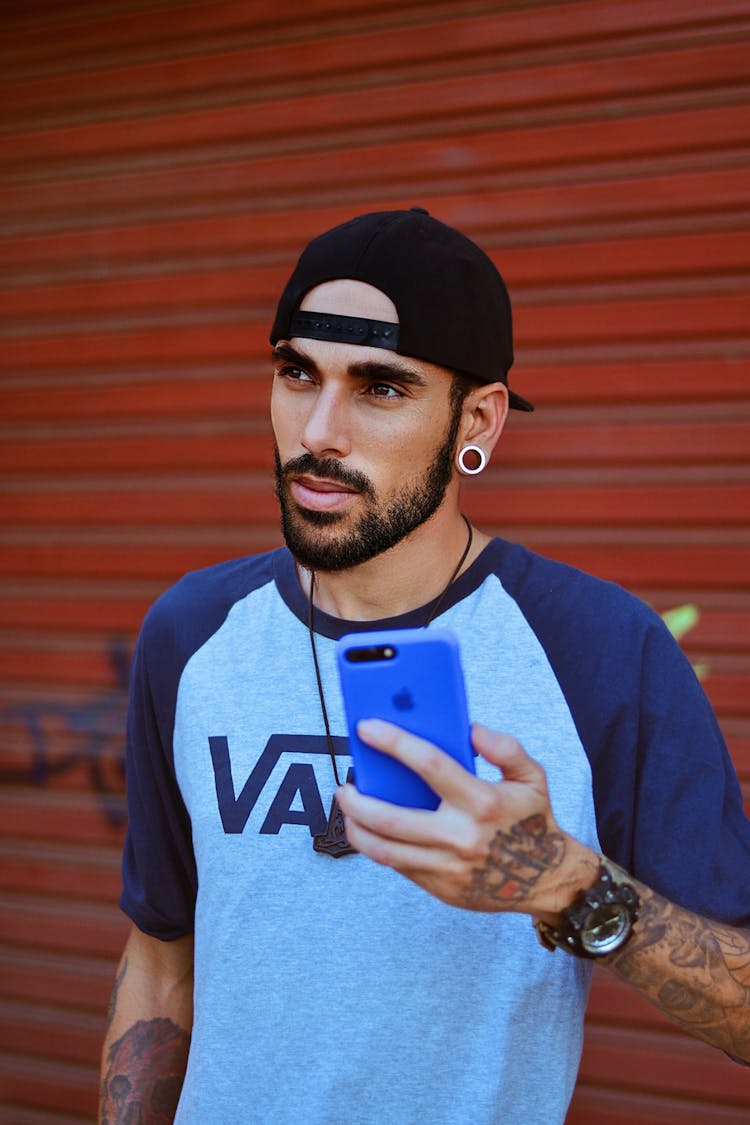 Man Wearing Black Cap Holding A Phone With Blue Case 