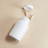 An unlabelled white bottle tipped over with capsules spilling out. Photo by Supplements On Demand on Pexels.
