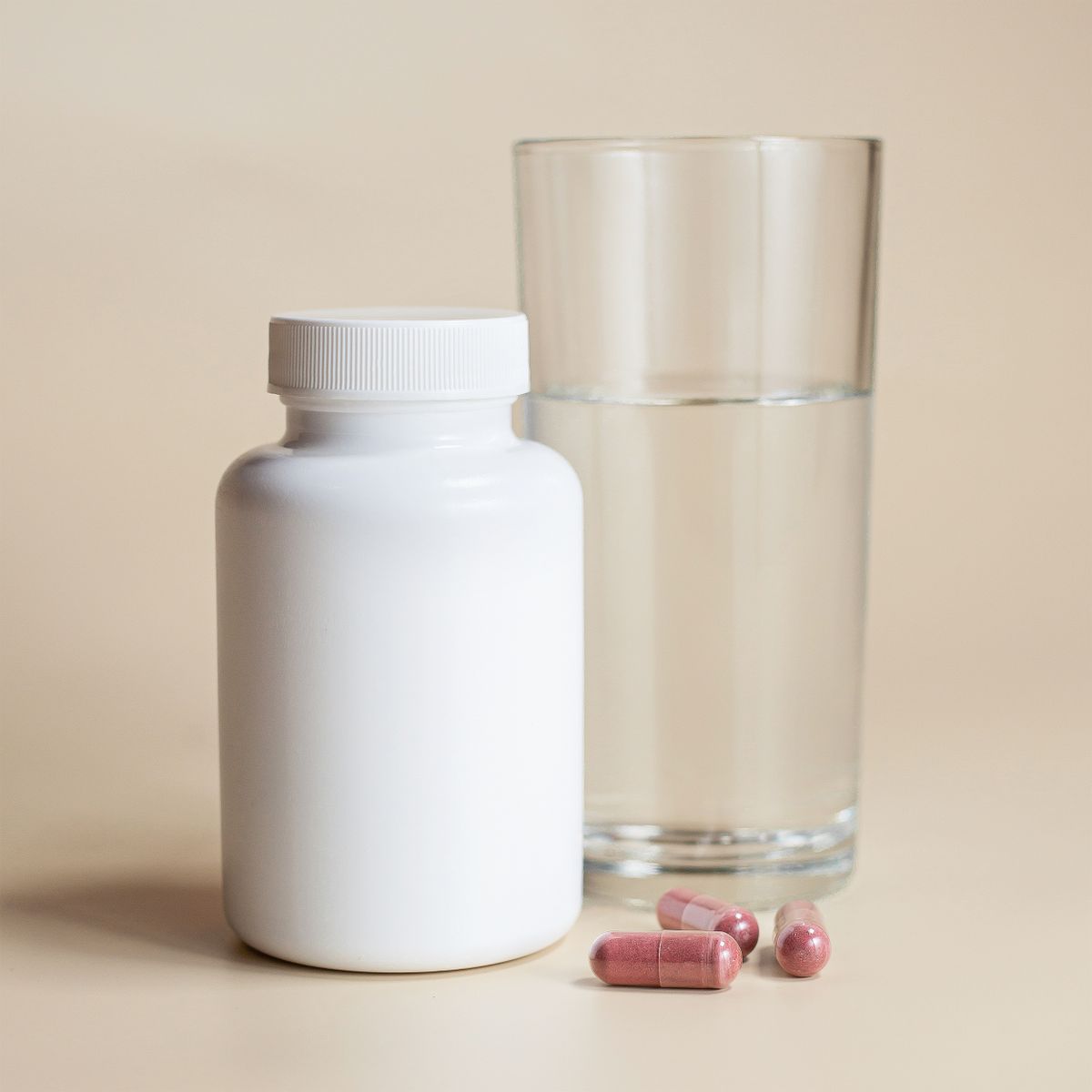 A sealed white supplement bottle beside a glass of water, representing a daily foundation routine