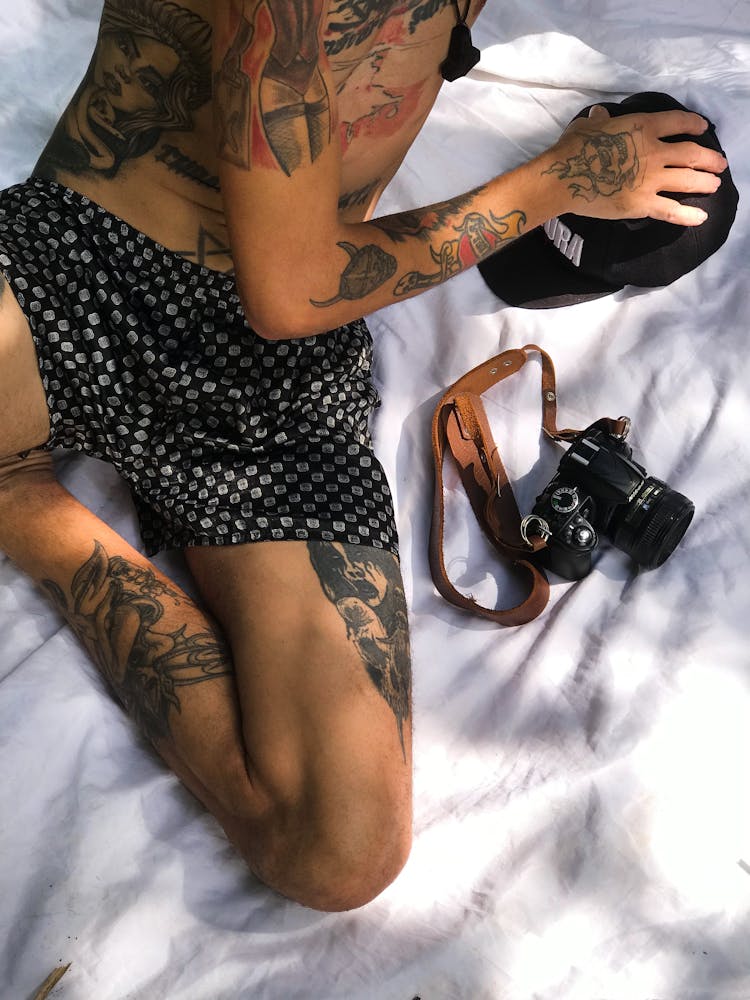 High Angle Shot Of Tattooed Man Sitting On White Cloth Beside A Camera 