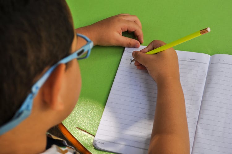 Close-Up Shot Of A Kid Writing On Notebook Using A Pencil