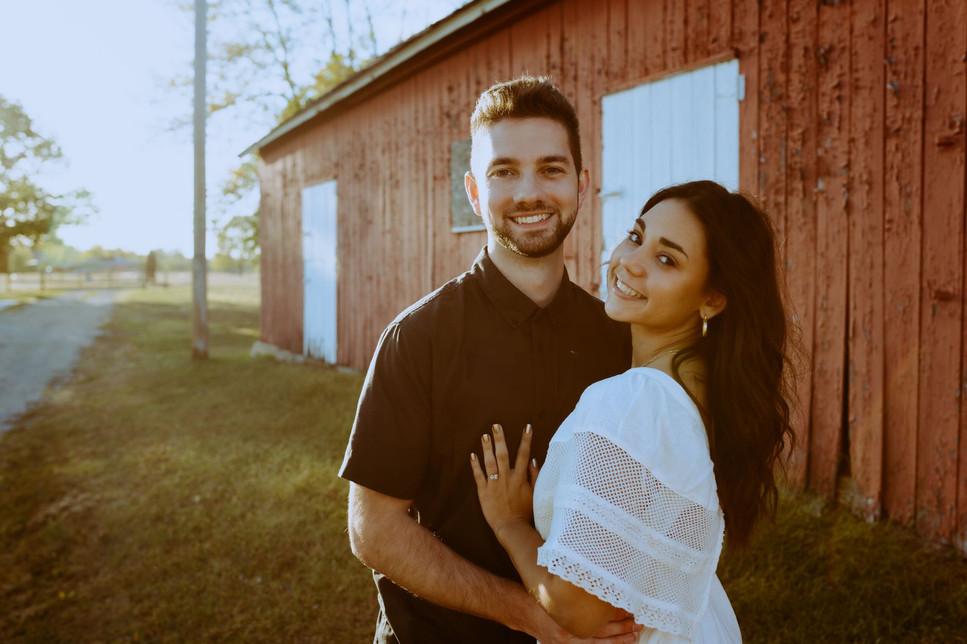 Happy couple embracing outdoors near a rustic barn, basking in warm sunlight.