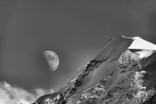Free Black and white photo of a snow-covered mountain with a half moon in the sky. Stock Photo