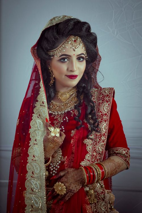 Free A stunning bride in lavish red and gold Indian attire, captured in a traditional wedding setting. Stock Photo
