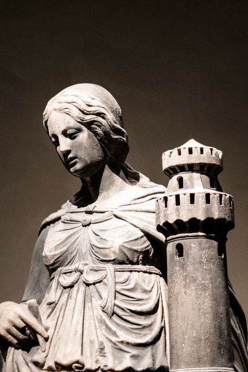 Free Classic stone sculpture of a woman dressed in flowing robes beside a tower. Stock Photo