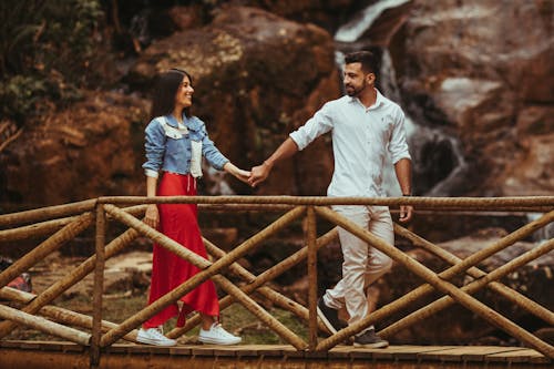 A Couple Holding Each Others Hands while Walking on a Wooden Bridge