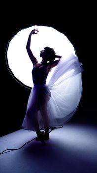 A graceful ballerina posed against a bright studio light, creating dramatic silhouettes.