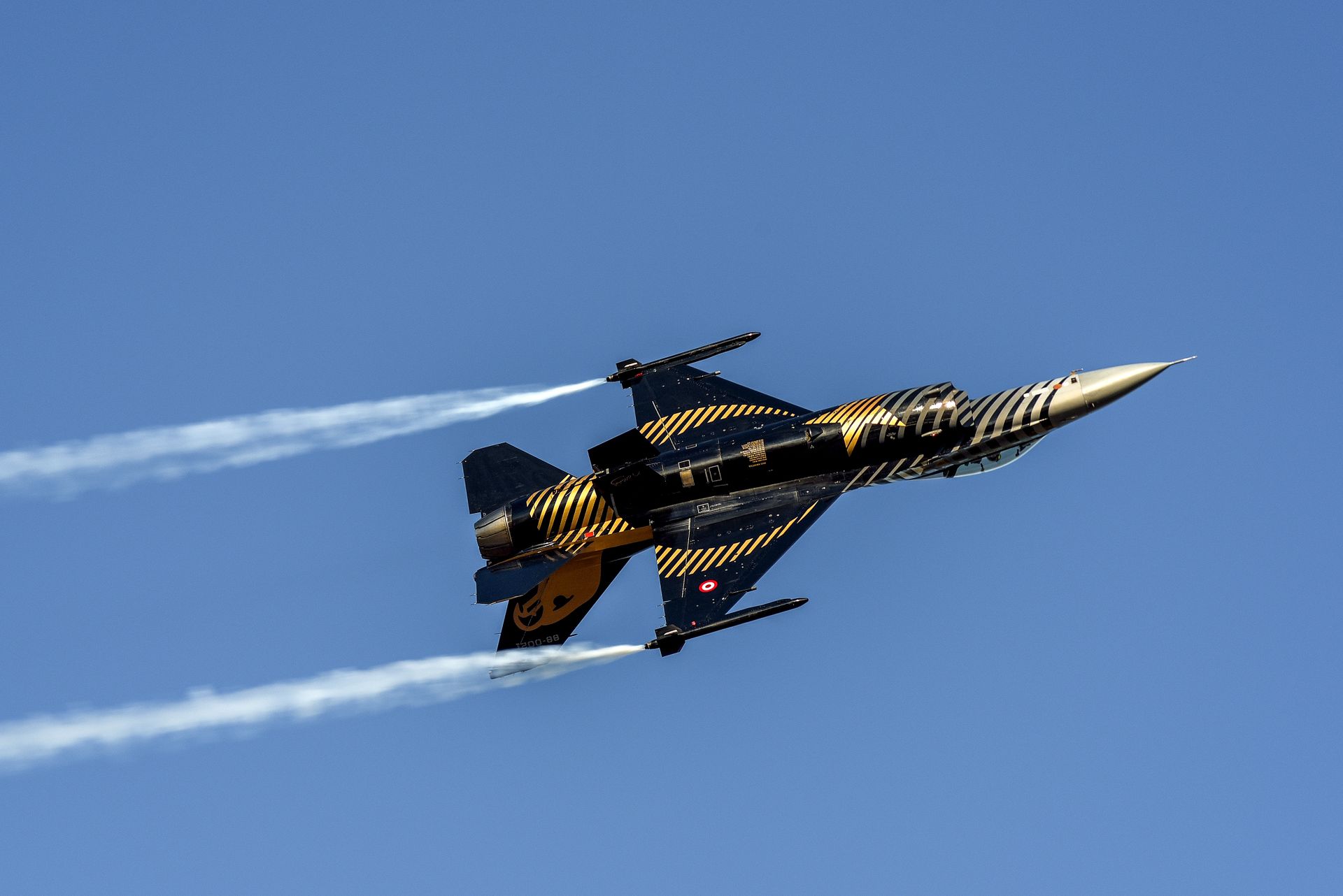 A military jet performing high-speed maneuvers against a clear blue sky, showcasing its agility and power.