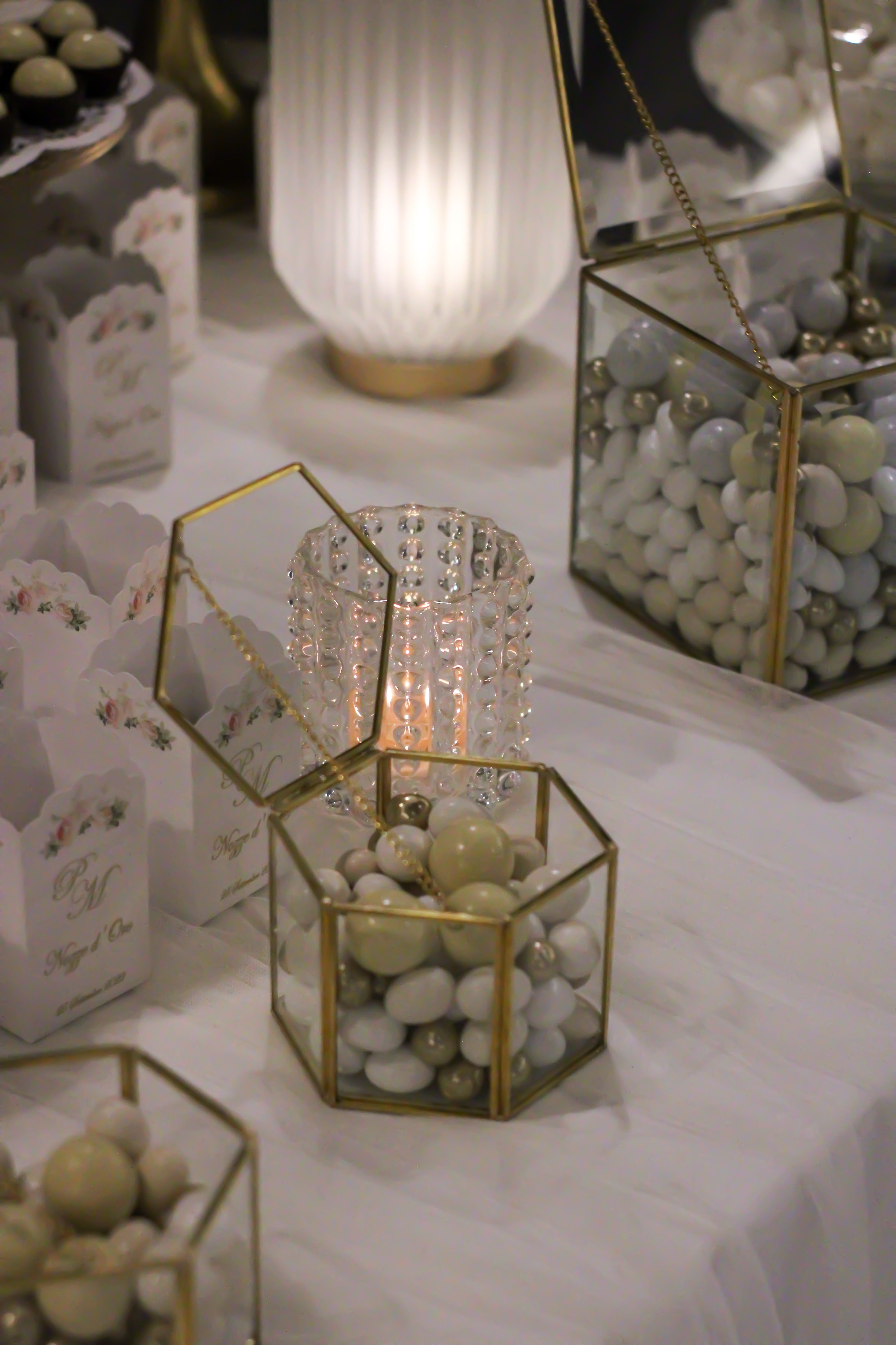 Luxurious wedding table setup featuring geometric boxes with candies and a glowing candle.