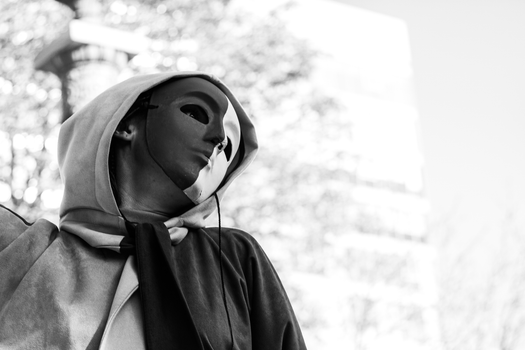 Black and white photo of a person wearing a mask and hoodie, evoking mystery.