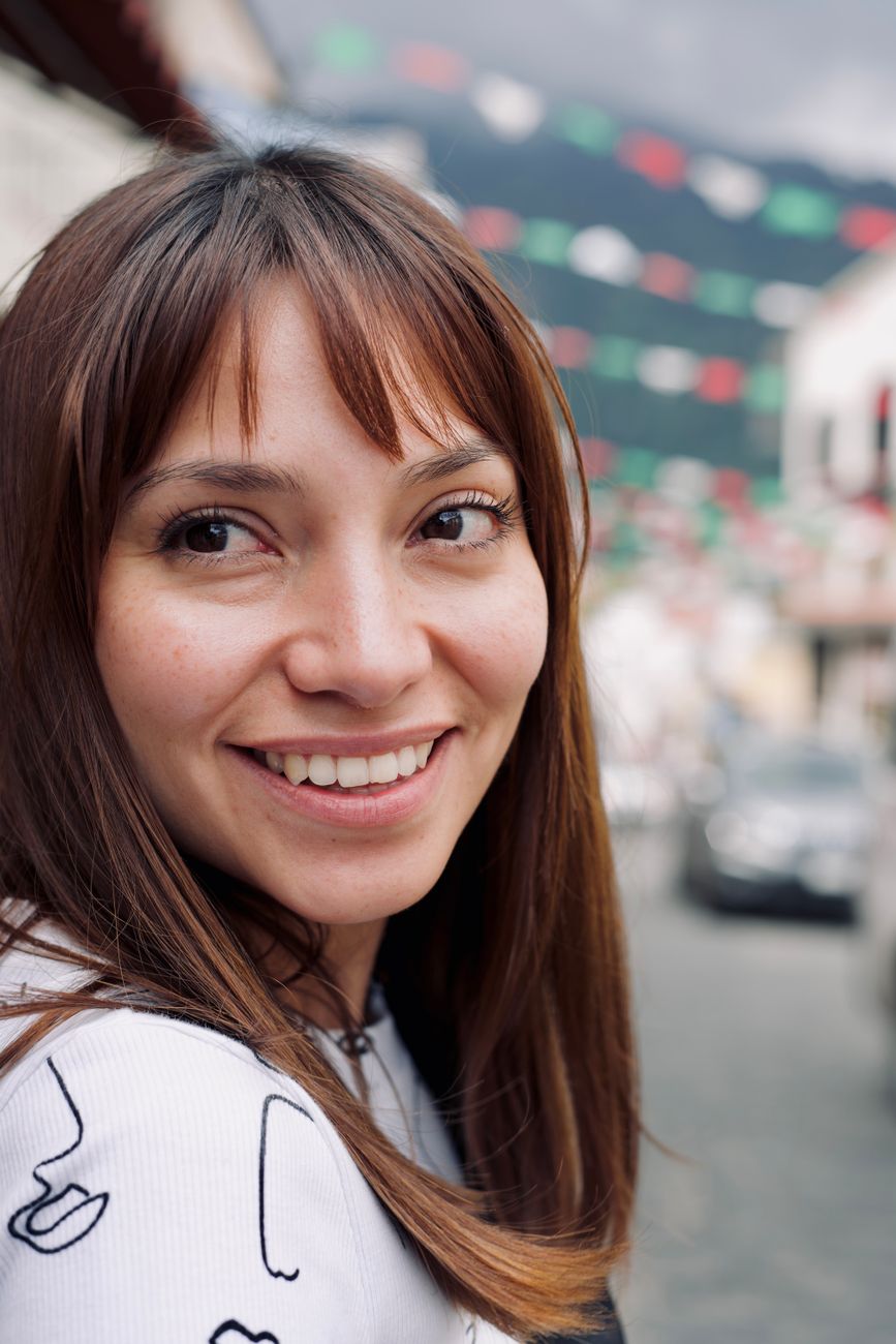 Portrait of a smiling woman with brown hair outdoors in Tepoztlán, Mexico under festive street decorations.